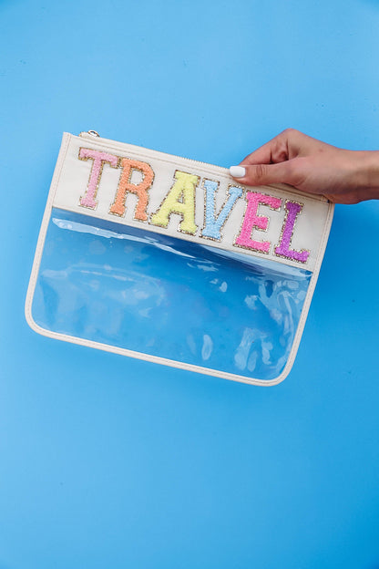 hand holding clear nylon bag with cream trim and chenille patches that spell "travel".