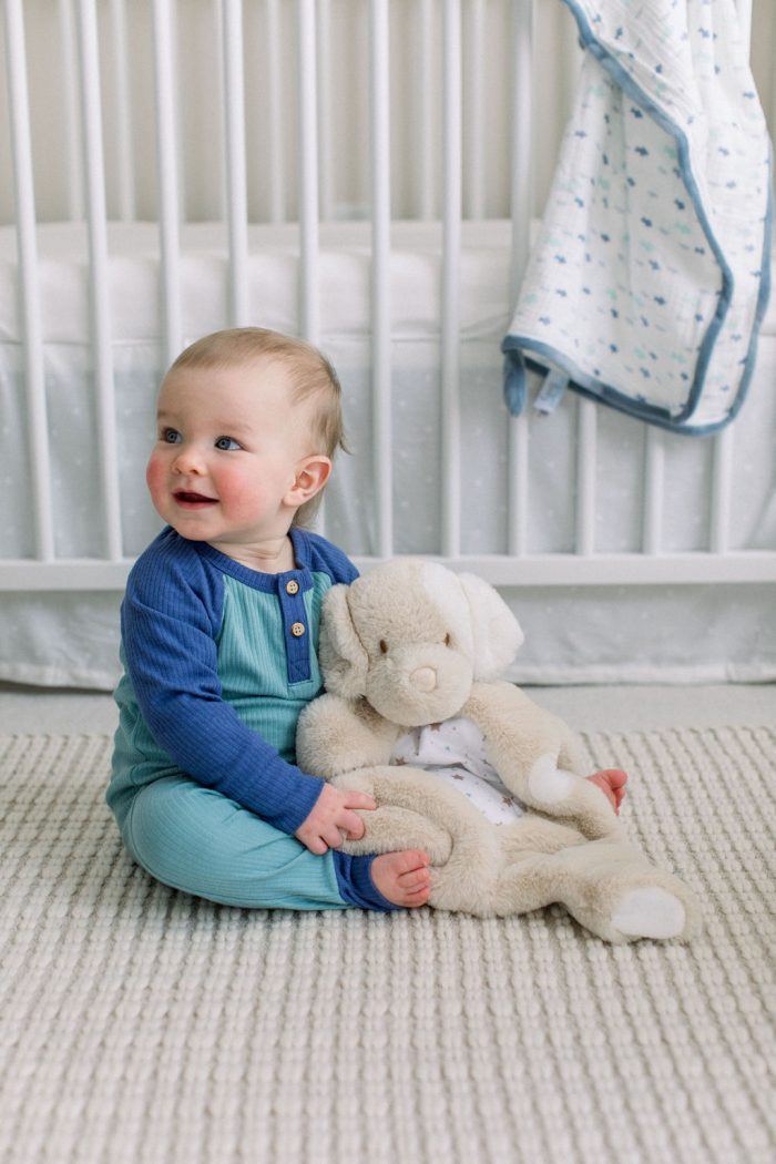 a baby boy sitting in front of a crib on the floor holding auggie tan puppy sshlumpie