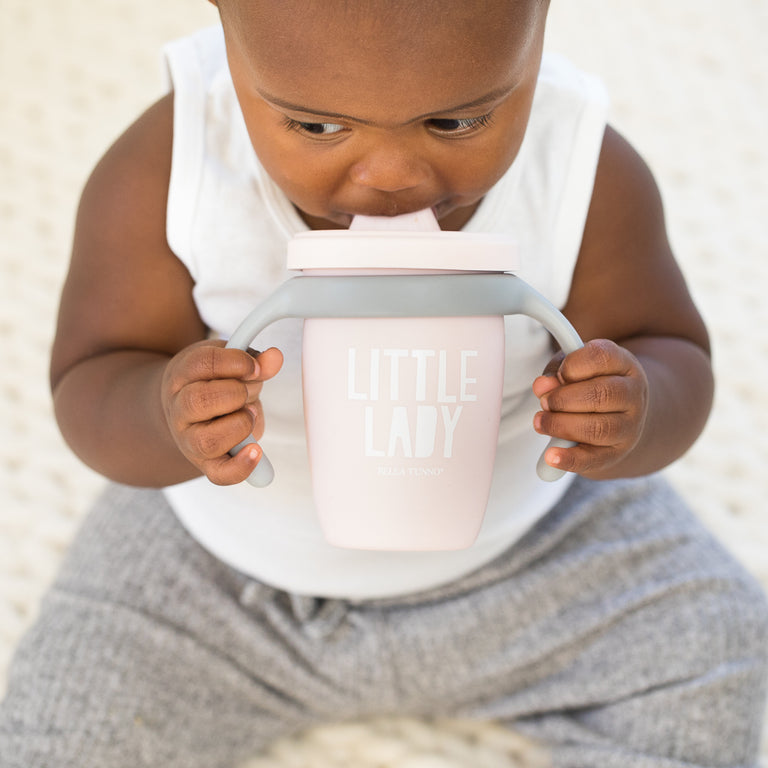 little girl sitting holding the happy sippy cup against a white background