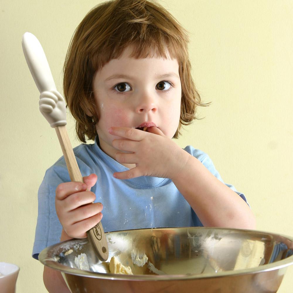 child sitting with a bowl of batter and holding the batter finger spatula.