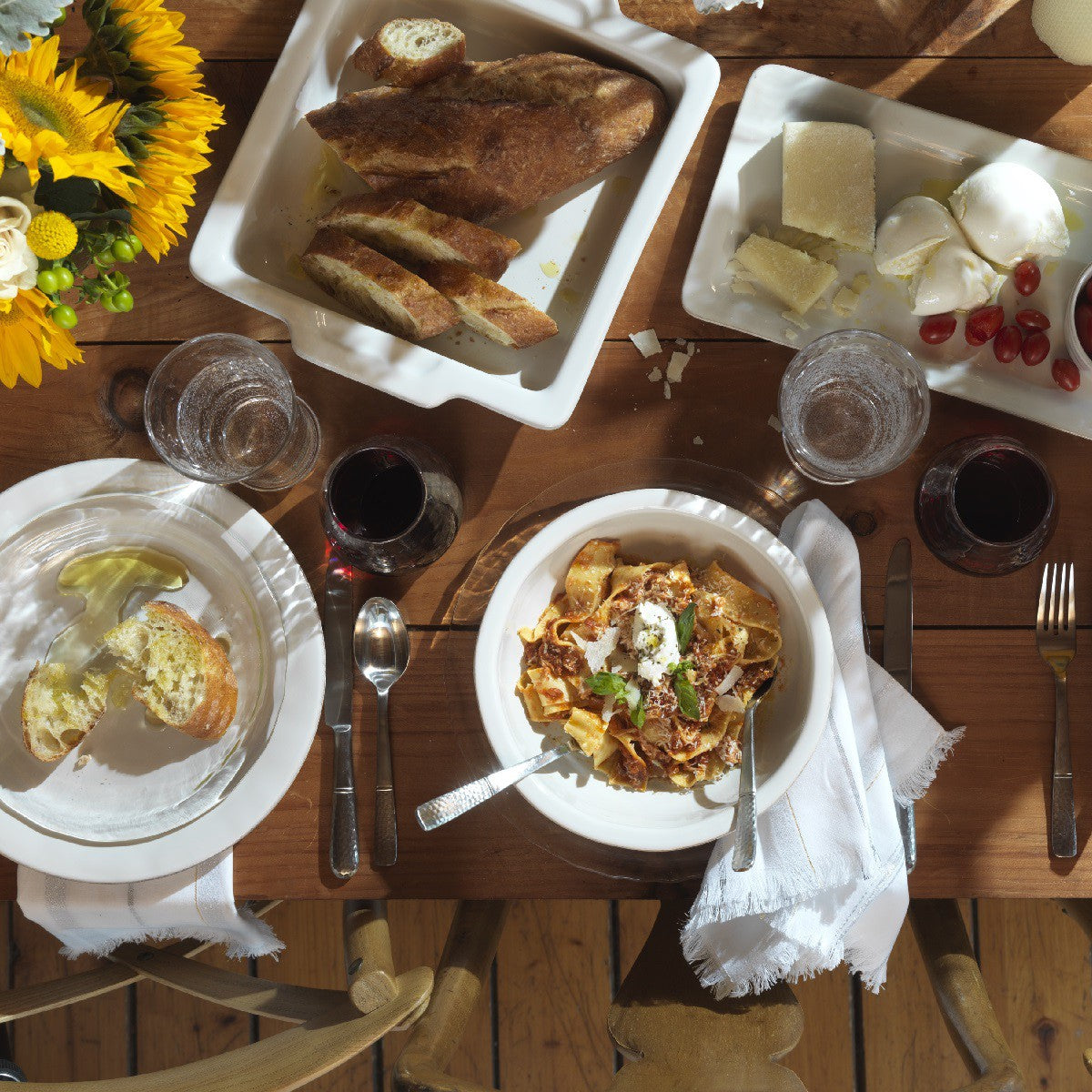 table setting on a rustic wood table with serving pieces, sunflower arrangement, glasses and flatware.