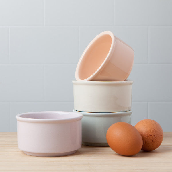 4 colors of ramekins stacked on a counter with 2 brown eggs.