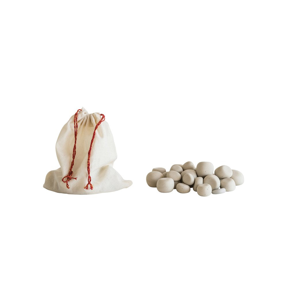 a pile of white pebbles next to a muslin bag on a white background