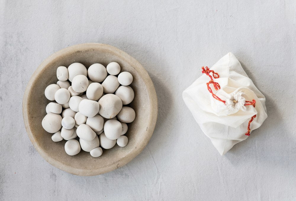 white pepples displayed in a wood bowl next to a muslin bag on a light gray background