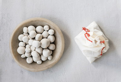 white pepples displayed in a wood bowl next to a muslin bag on a light gray background