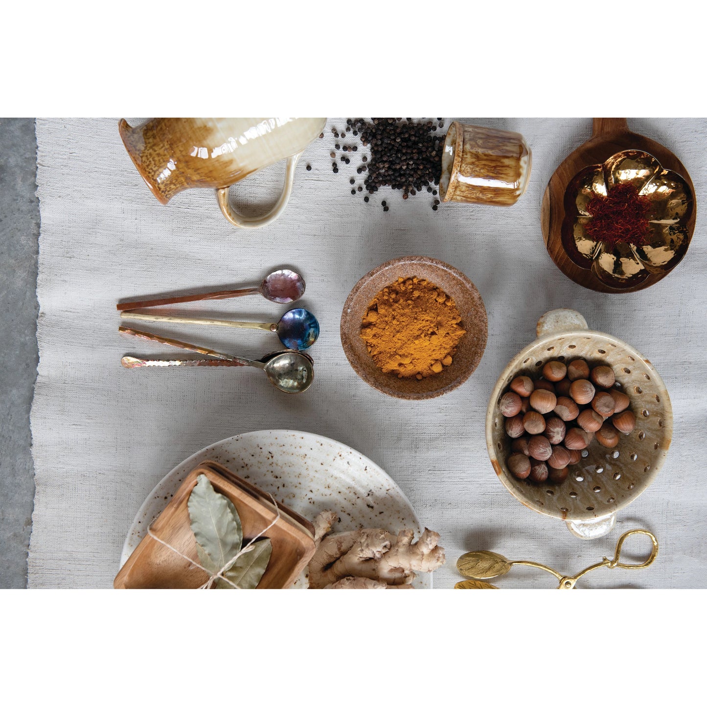 top view of a table setting with four burnt copper spoons, berry bowl spices, pitcher and serving bowls on a white tablecloth