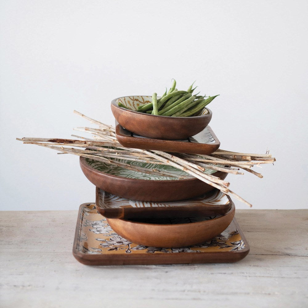 square enameled acacia wood trays stacked with enameled wood bowls and veggies on a light wood surface against a white background