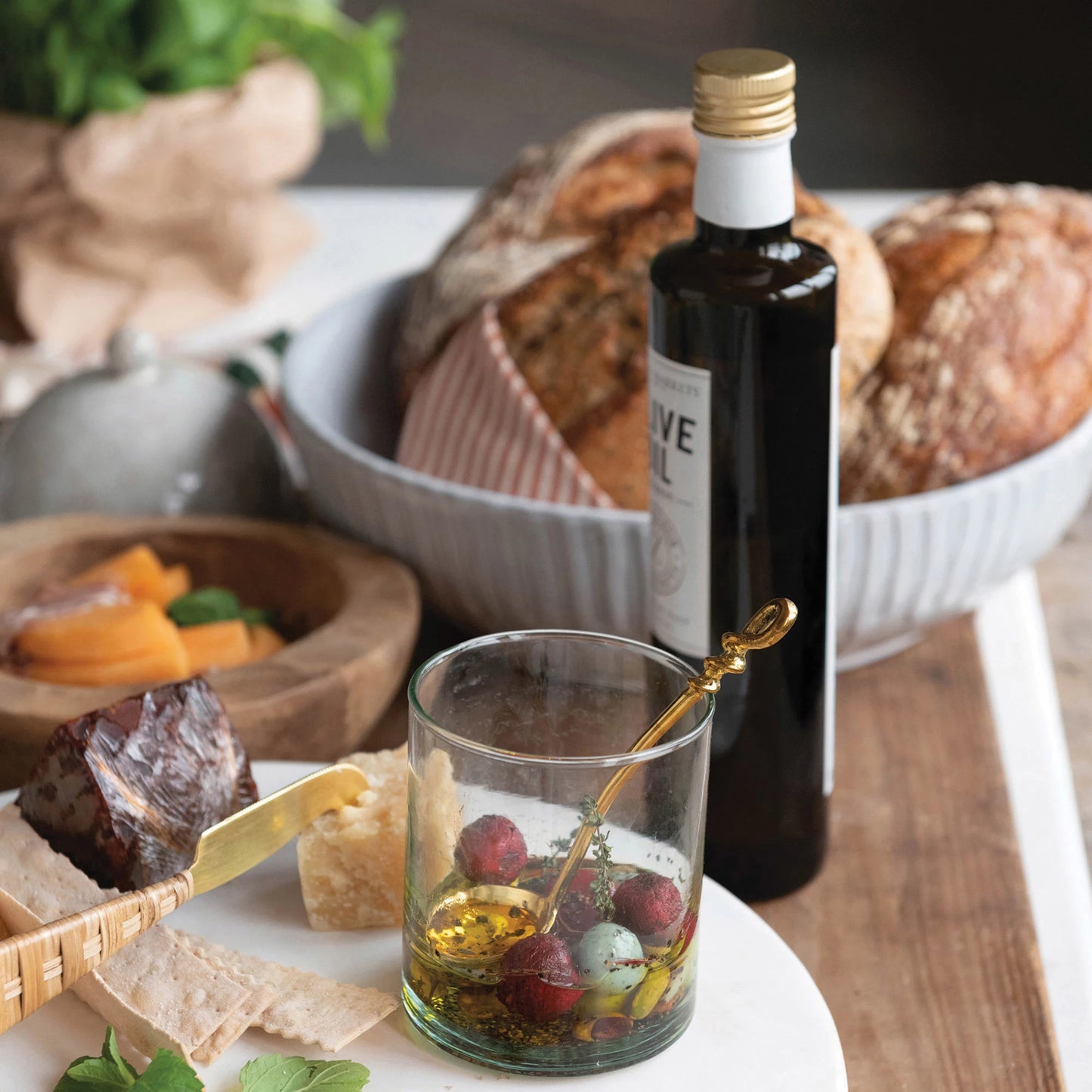 table setting with the debossed stoneware bowl with bread bottle of oil olives cheese slices and greenery on a white table
