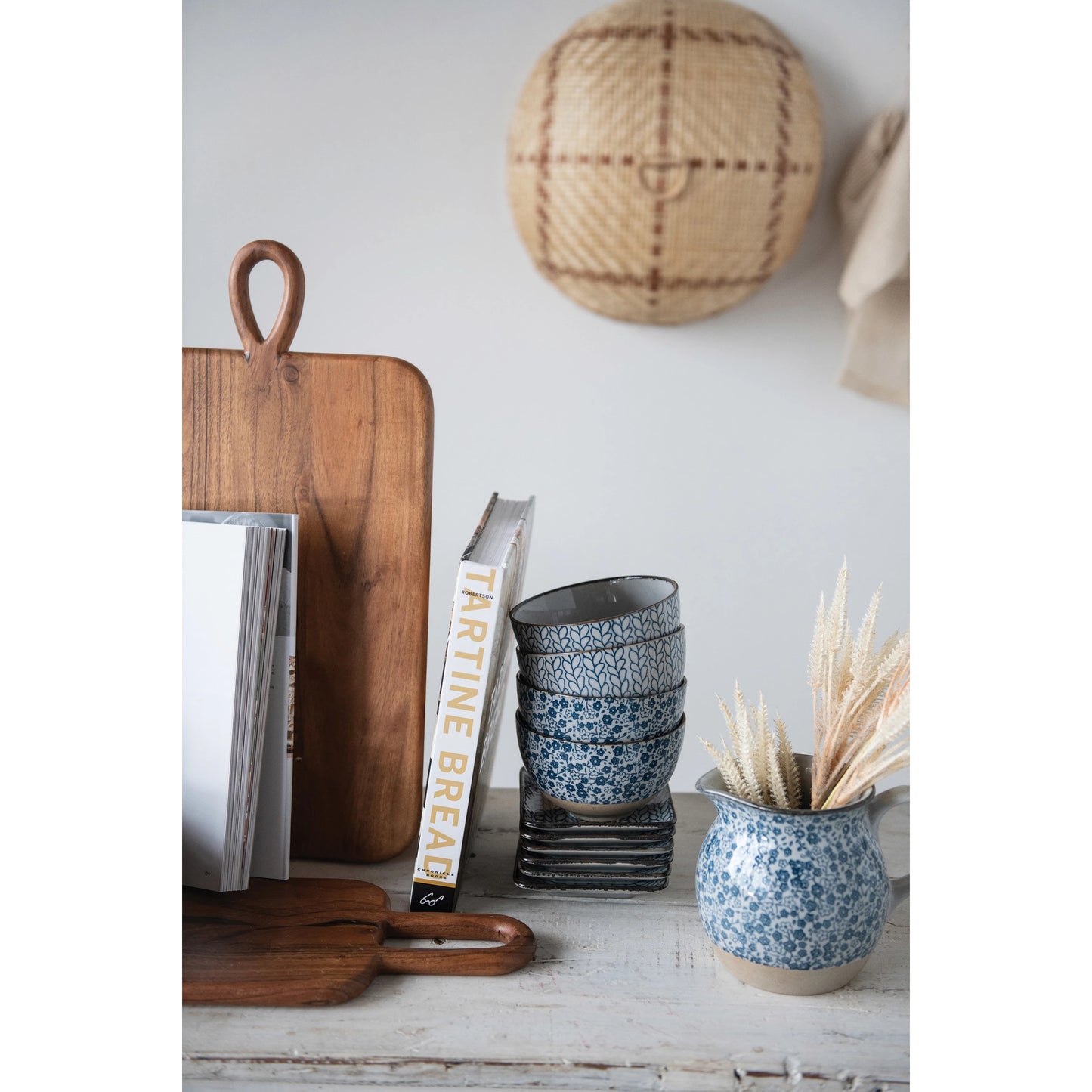 stack of bowls, books, and a pitcher filled with dried grasses on a wooden countertop.