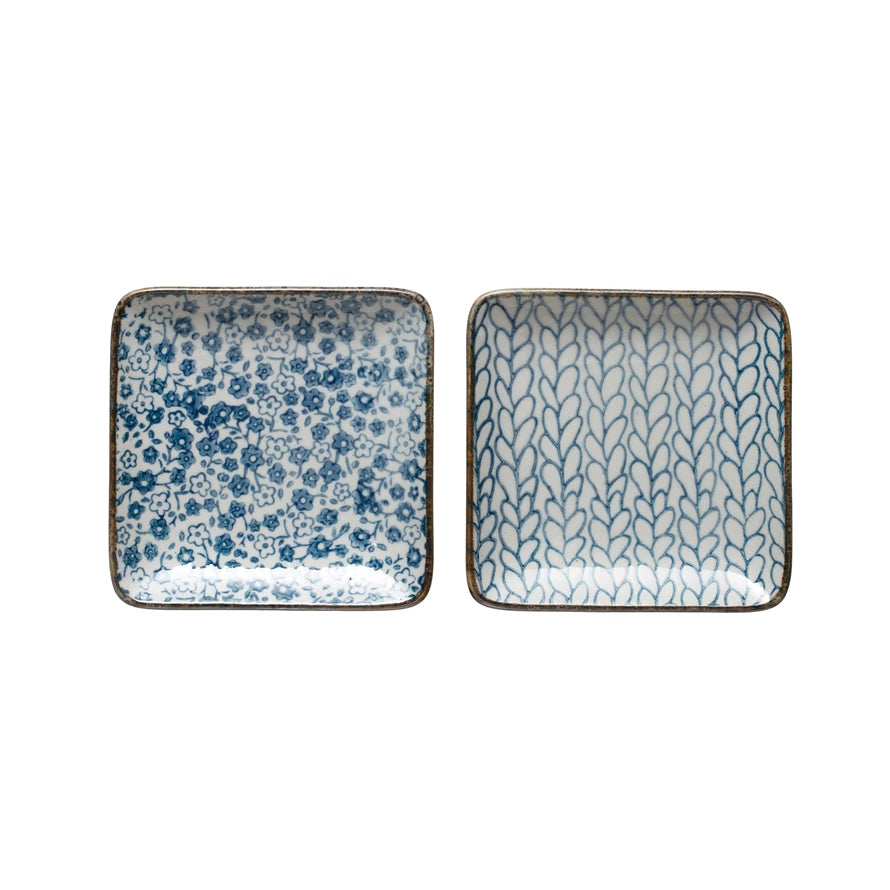 2 square off-white plates, one has blue floral pattern, the other has a vining leaf pattern.