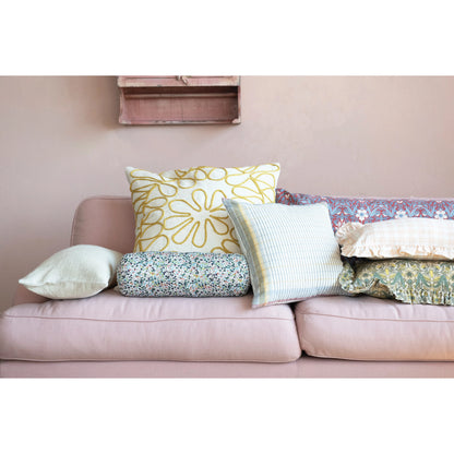 the dark gold embroidered slub pillow displayed on a pink sofa with multiple floral pillows surrounding 