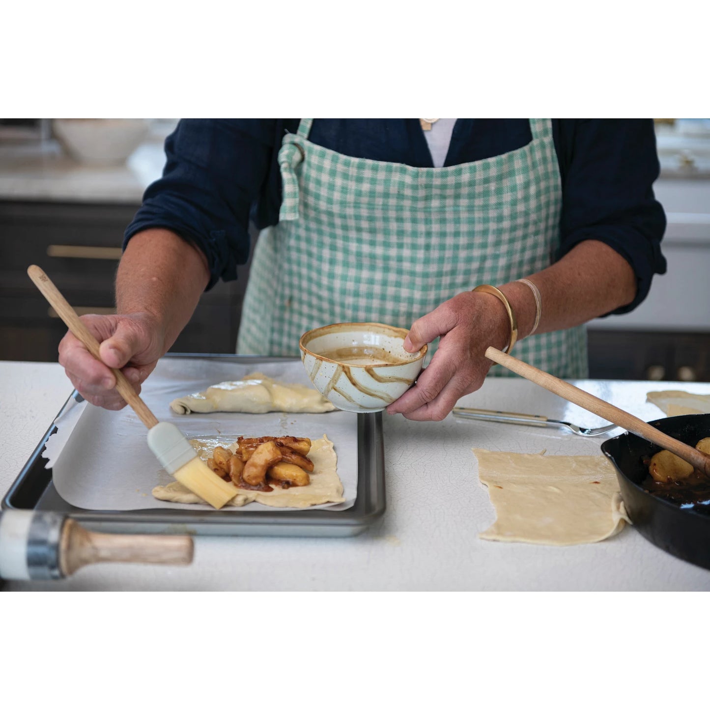 a woman working in a kitchen wearing a turquoise and white checked apron filling pastries