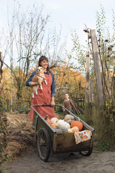 person wearing apron, holding dog, and pushing wagon.