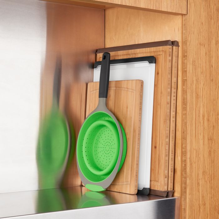 collapsed colander stored in cabinet with cutting boards.