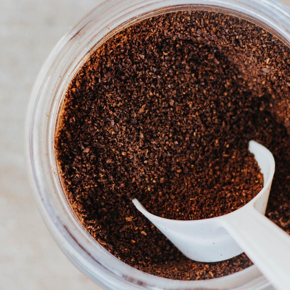 top view of a coffee jar filled with ground coffee and a white coffee scoop