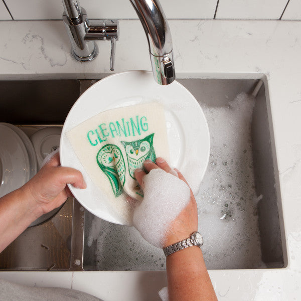 a persons hands washing a dinner plate in a sing of soapy water with the hootenanny swedish sponge cloth