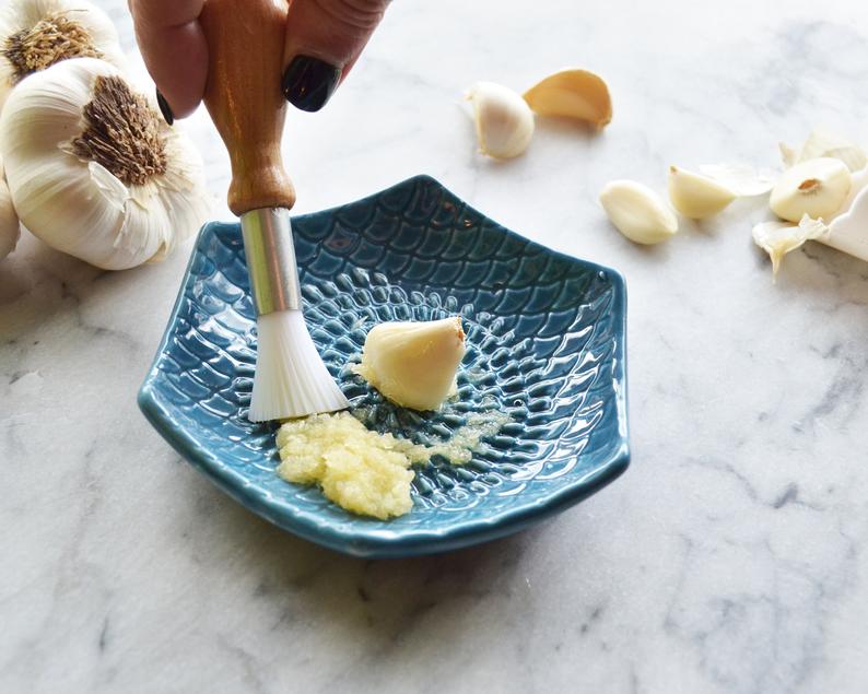hand brushing garlic off grate plate with garlic bulbs and cloves in background.