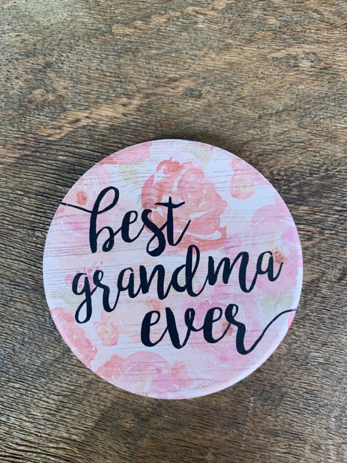 best grandma ever car coaster is white with pale pink flowers and black text displayed on a wooden background