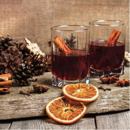 two hot cranberry cider drinks displayed next to acorns, star anis, and dried orange slices