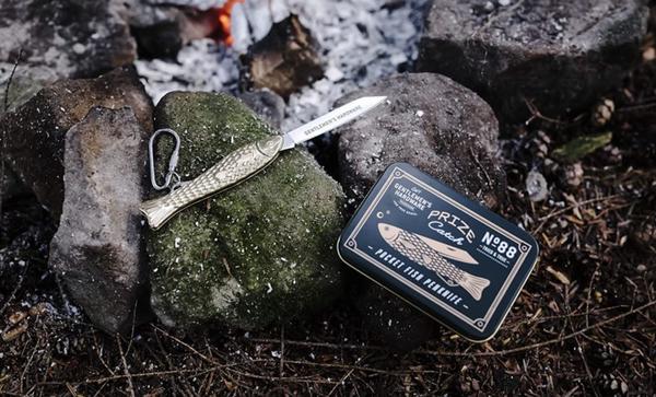the pocket fish knife displayed on a rock by a campfire with the tin box sitting beside it