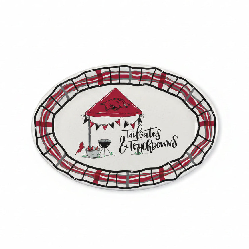An oval serving platter featuring a red and black plaid border, a central illustration of a red tailgates tent with the Arkansas Razorbacks logo, a grill, and the text 'Tailgates & Touchdowns' in black script