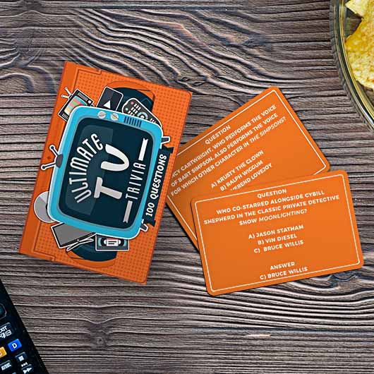 the ultimate tv trivia package displayed next to two trivia cards on a dark stained wood table