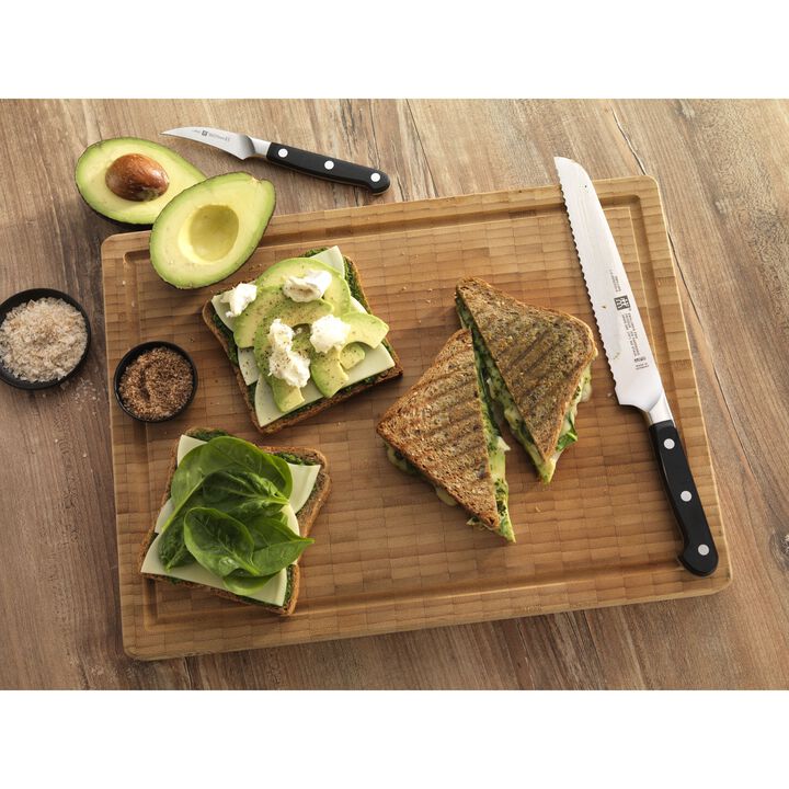 PRO 8 Inch Bread Knife laying on a wooden board with sandwiches, avocado slices, and seasonings.