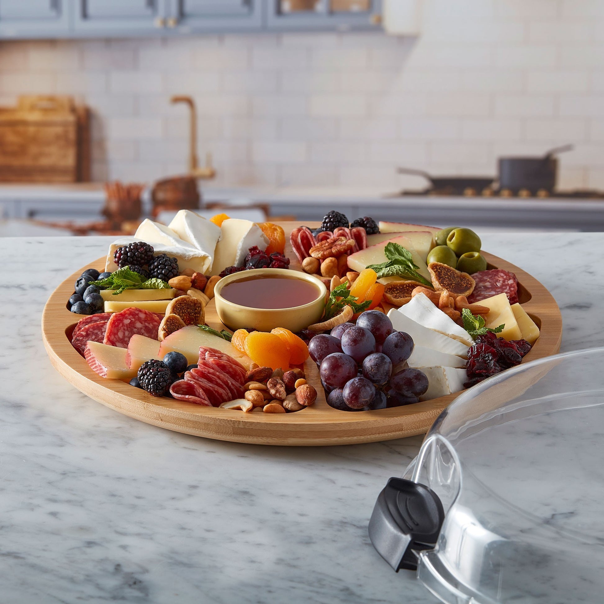 Round Build a board filled with fruit, meats and cheese set on a counter with the lid next to it.