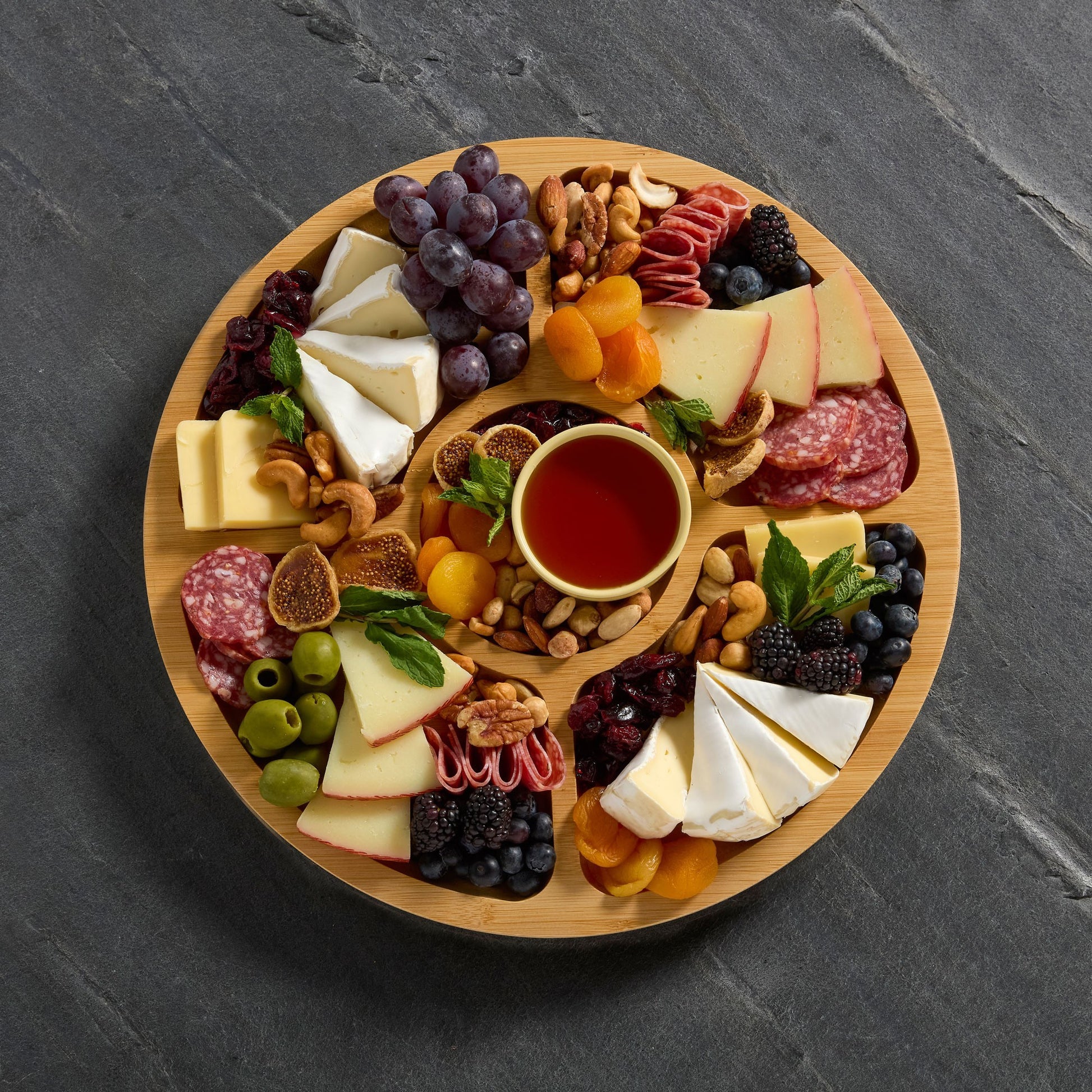 Top view of round builder board filled with meat, cheese and fruit Set on a Gray slate background.