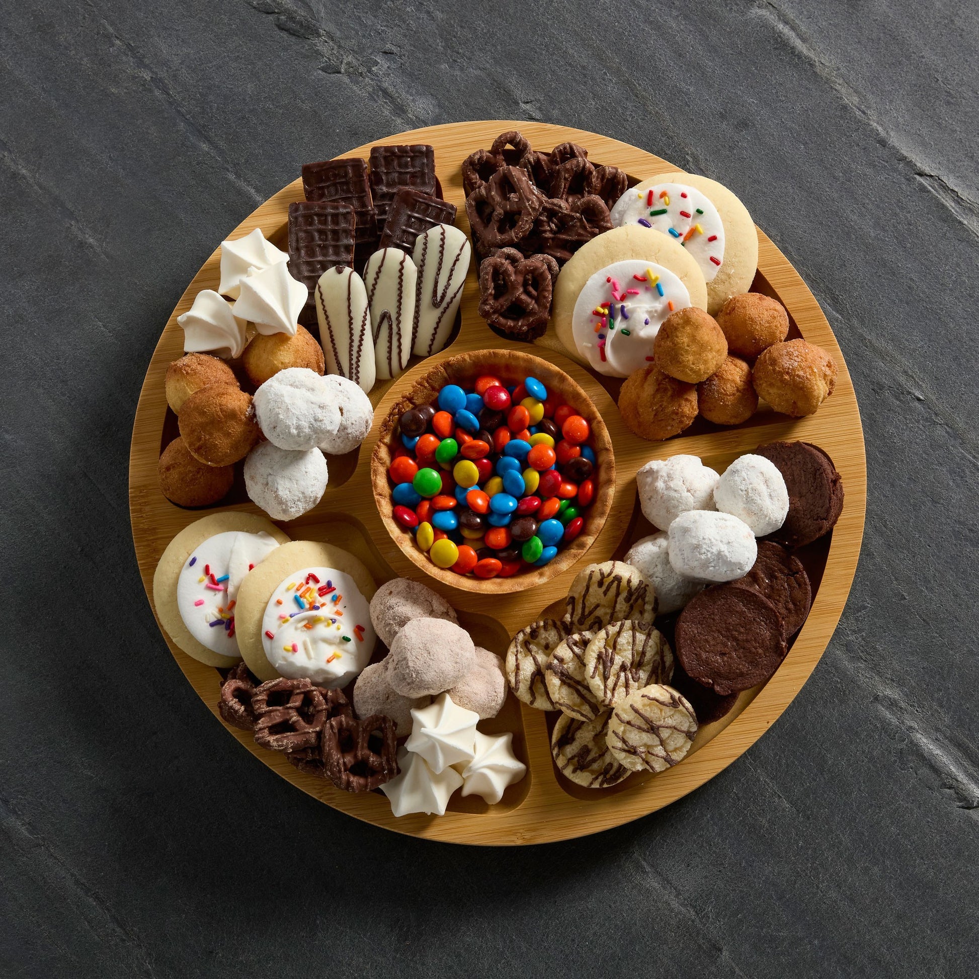 Top view of round builder board filled with cookies and candies set on a Gray slate background.
