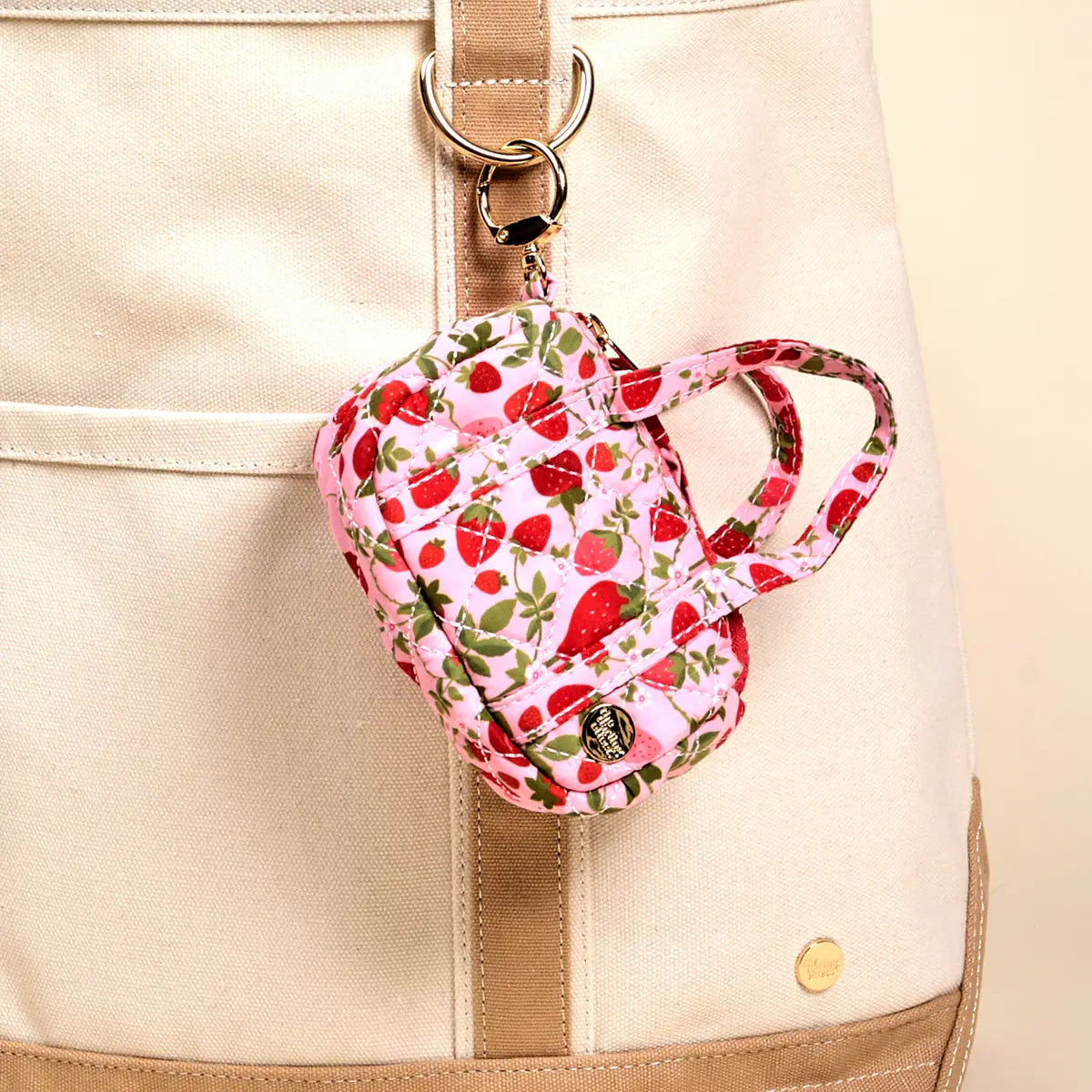 tiny duffle bag with strawberry pattern clipped to a beige and cream tote bag
