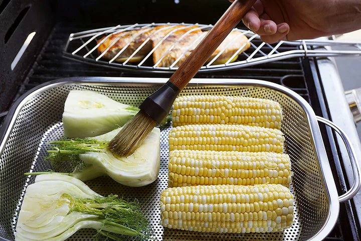 hand basting veggies in a BBQ Roasting Pan set on a grill