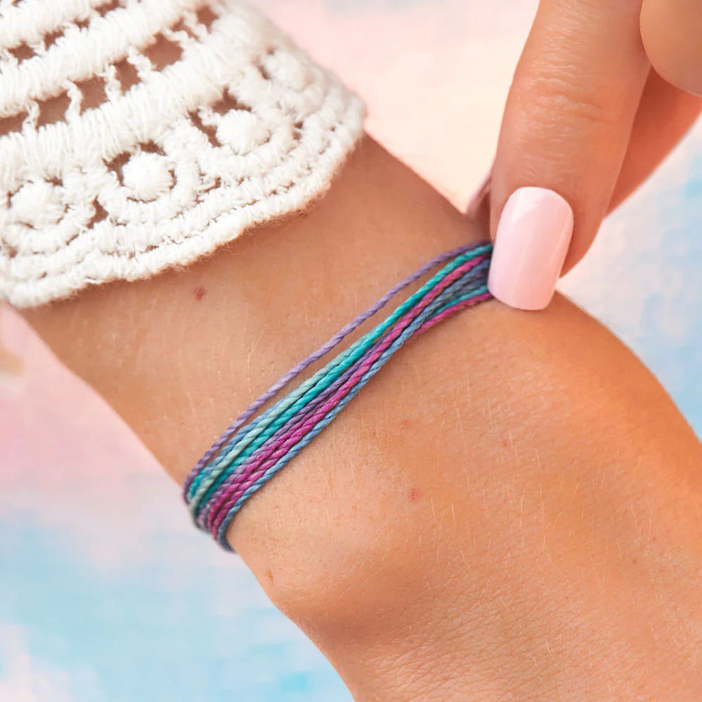 Pura Vida multi strand corded bracelet in varying shades of blue, pink, purple, cream with a Pura Vida logo charm on a wrist