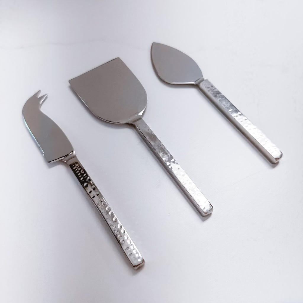 silver cheese knife, server, and fork on a white background.