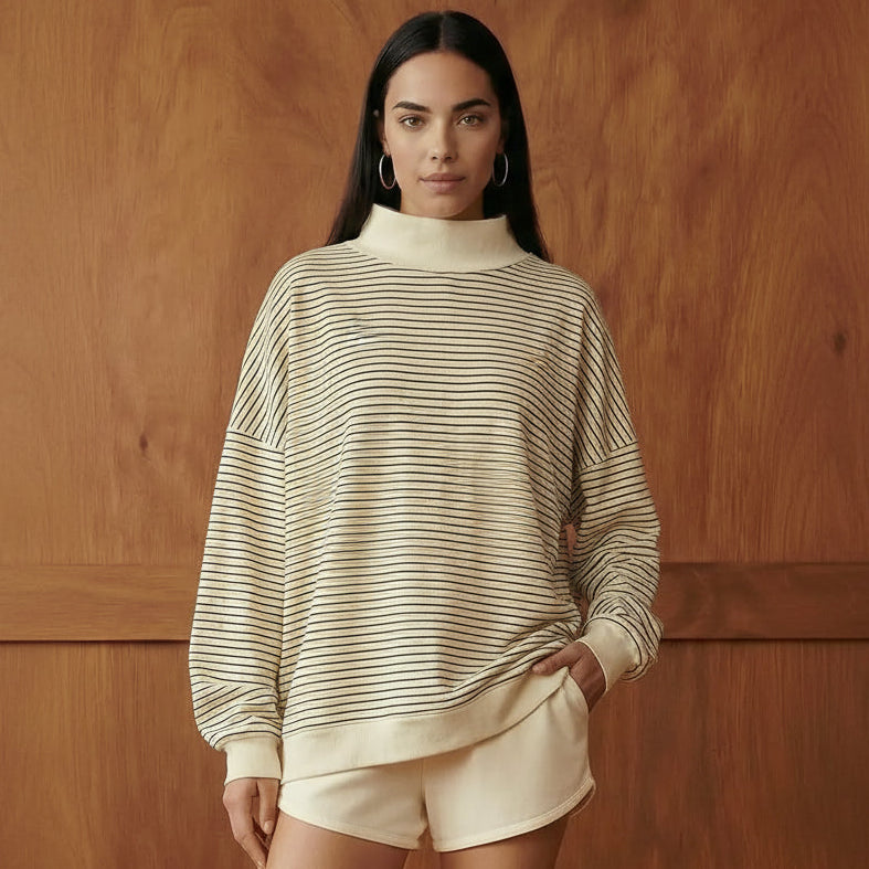 person wearing a cream with navy stripes mock neck sweatshirt standing in front of a wooden wall
