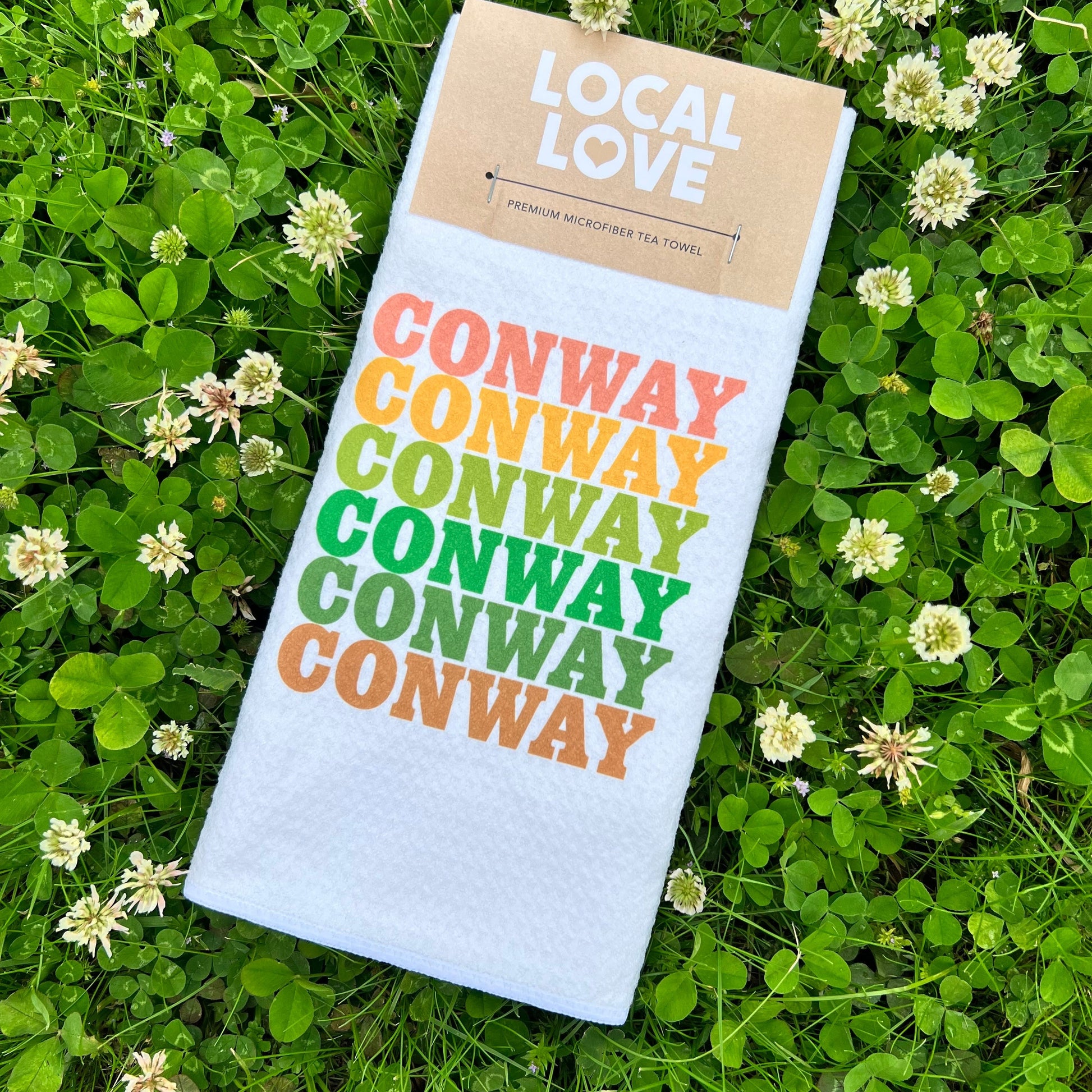 white towel with "conway" printed 6 times in assorted colors laying in a field of clovers.