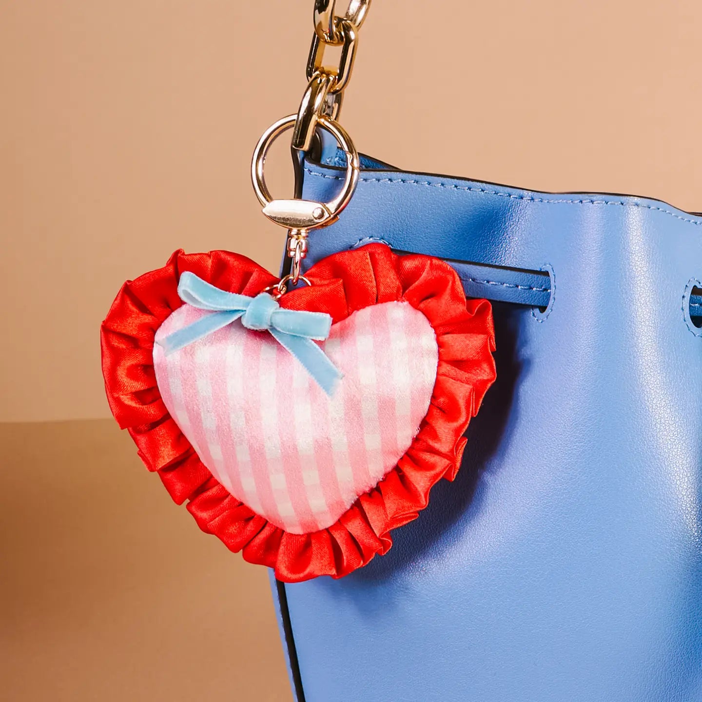 berry sweet Heart-shaped bag charm with red ruffles and a blue bow attached to a blue handbag.