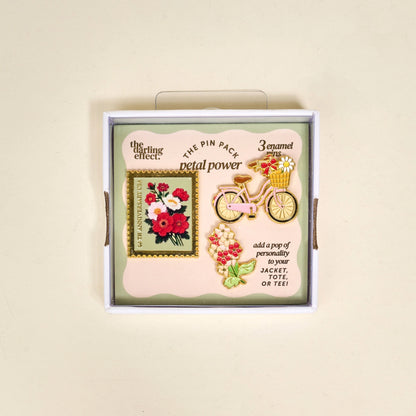 Packaged set of decorative pins with floral and bicycle designs in box packaging on a beige background