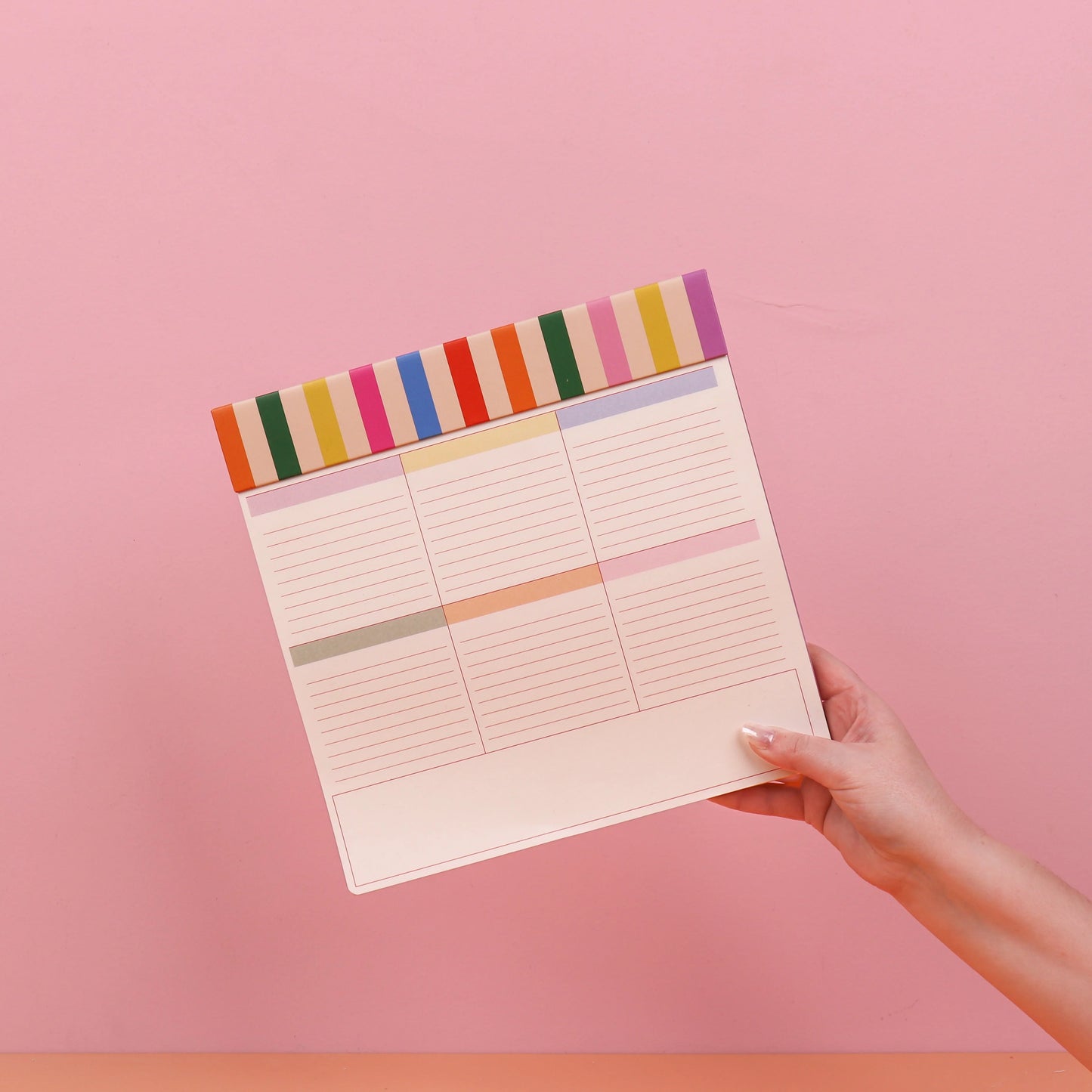 Notebook with colorful boarder held by a hand against a pink background