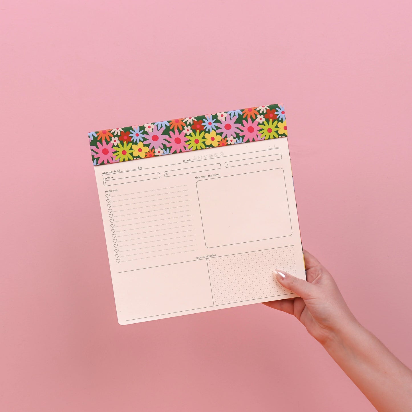 Hand holding a planner with a floral border on a pink background