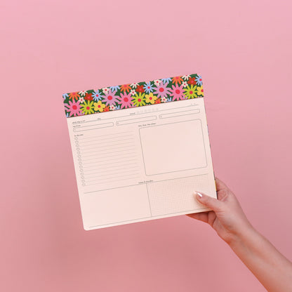 Hand holding a planner with a floral border on a pink background