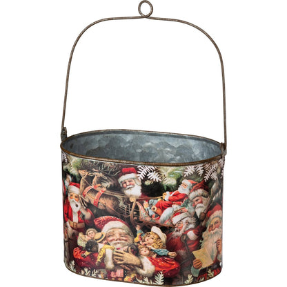 A vintage-style metal bucket with a handle, featuring a detailed Christmas print of Santa Claus and toys on the front, set against a plain white background.