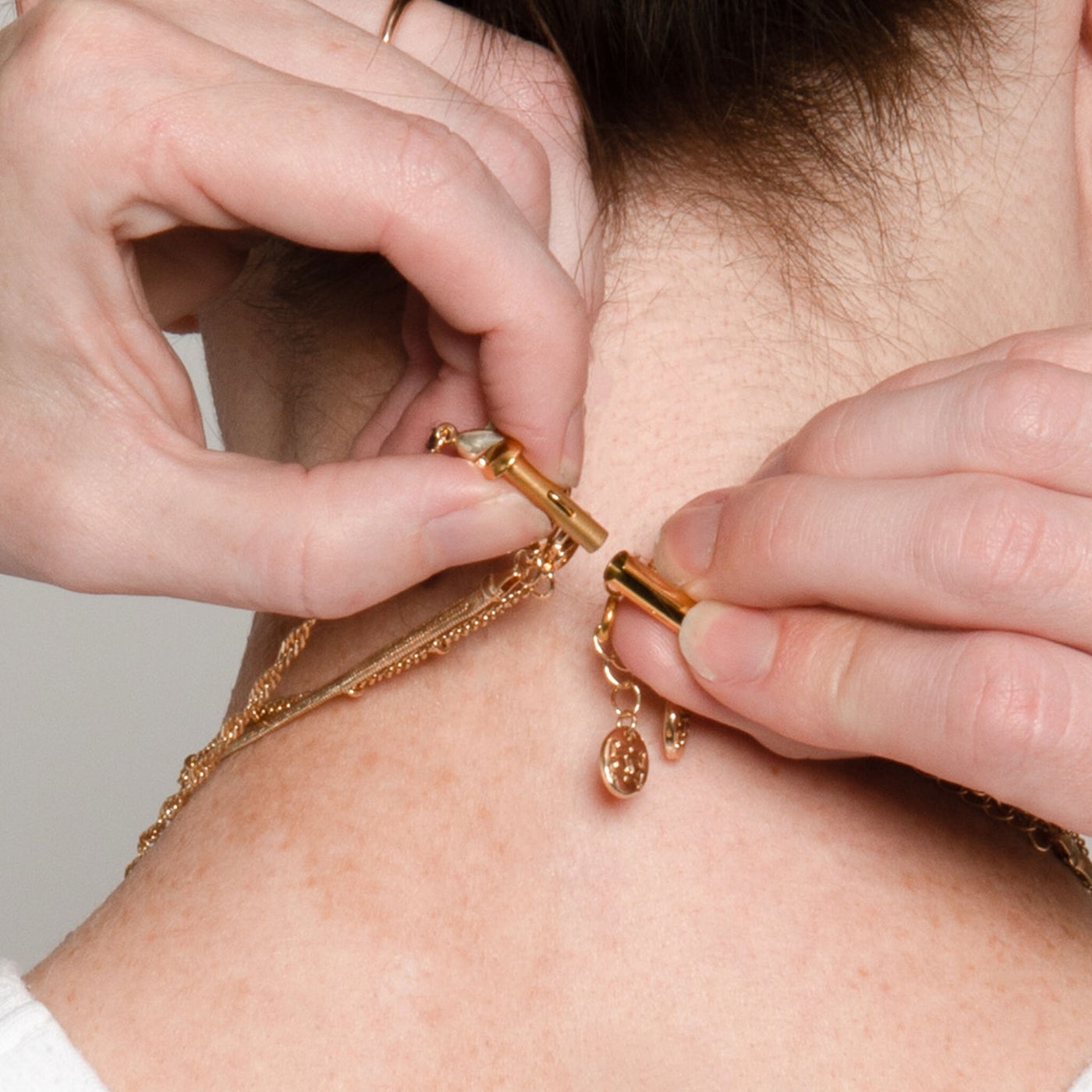 hands behind persons neck demonstrating the gold triple magnetic clasp.