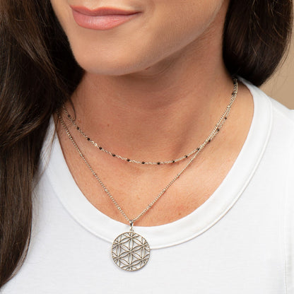 woman wearing silver chain with black beads and another silver chain with round pendant.