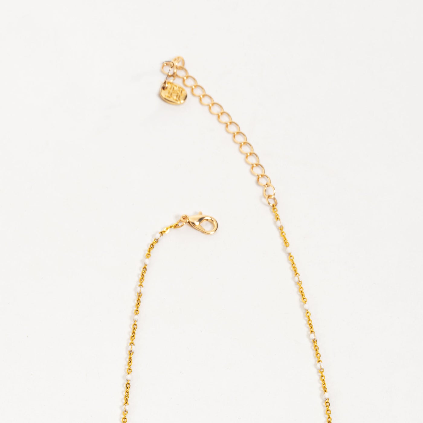 close-up of clasp on gold chain wit white beads.