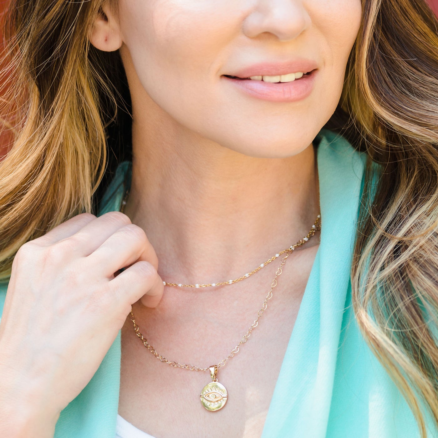 woman wearing gold chain with white beads and another gold chain with pendant.