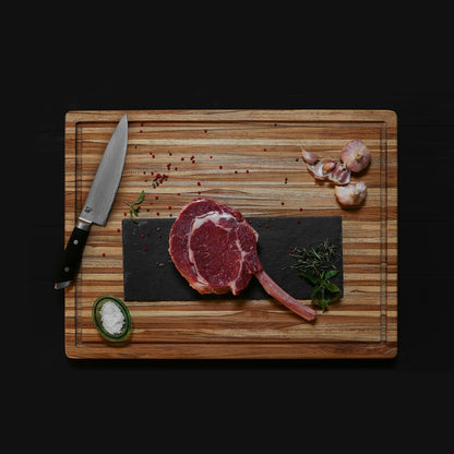 top view of carving board with a slab of meat, a knife, and herbs and spices on it.