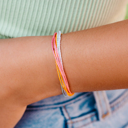 Pura Vida multi strand corded bracelet in varying shades of pink, white, and orange with a Pura Vida logo charm on a wrist