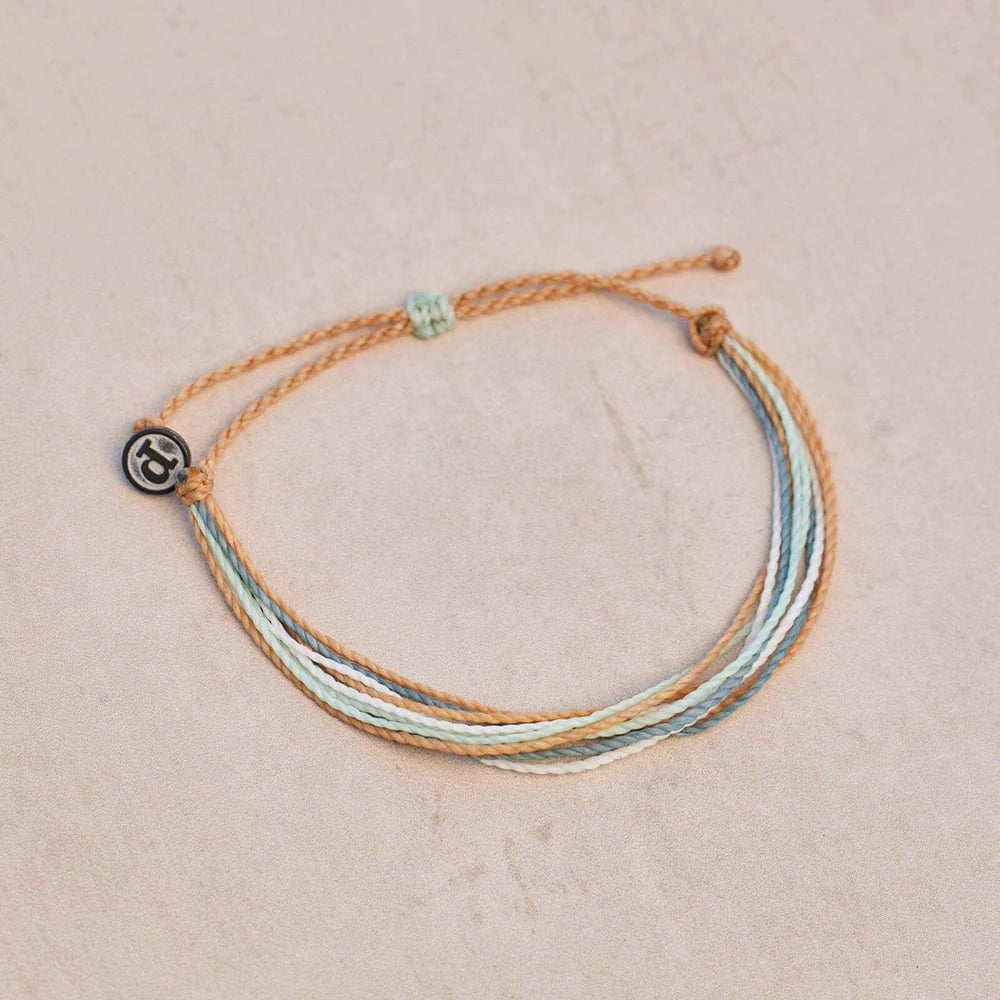 Pura Vida multi strand corded bracelet in varying shades of tan, white, and dusty blue with a Pura Vida logo charm