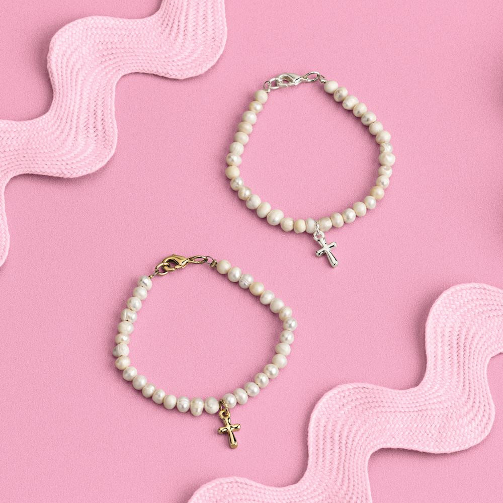 Two pearl bracelets with gold and silver cross charms on a pink wavy background
